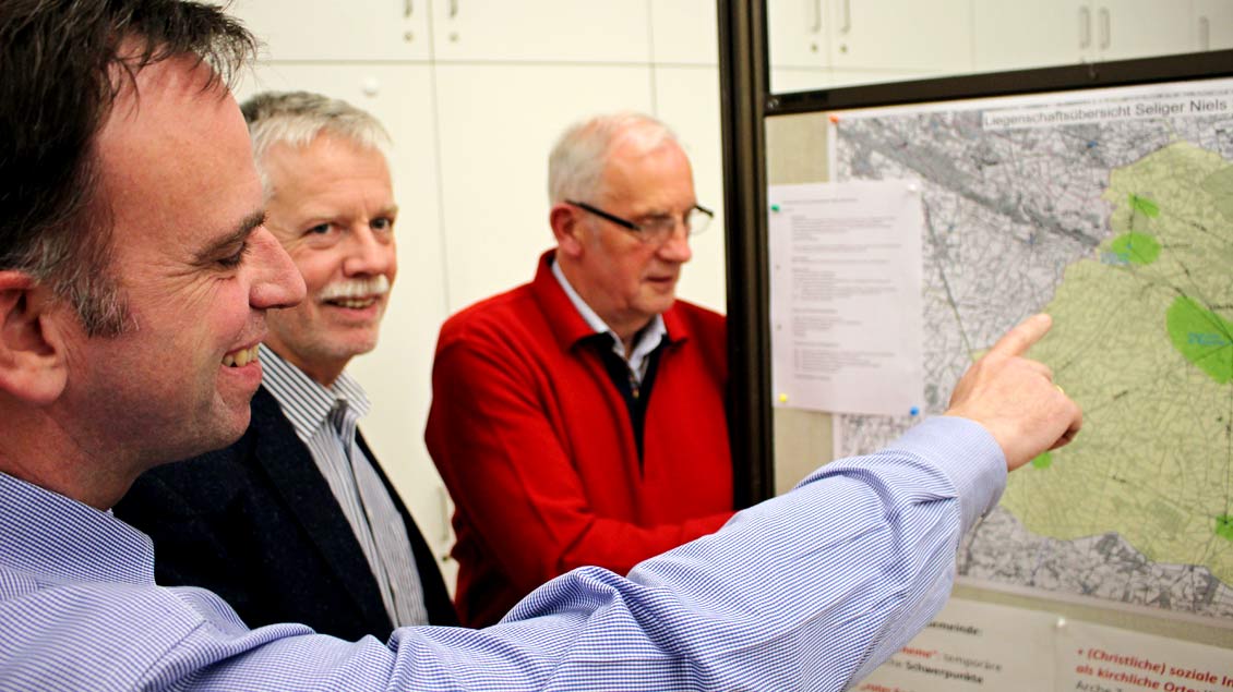 Michael Schüller (vorne links), Alexander Fenker und Alois Thomes aus der Steuerungsgruppe „Lokaler Pastoralplan“ erklären die Landkarte der Pfarrgemeinde Seliger Niels Stensen.