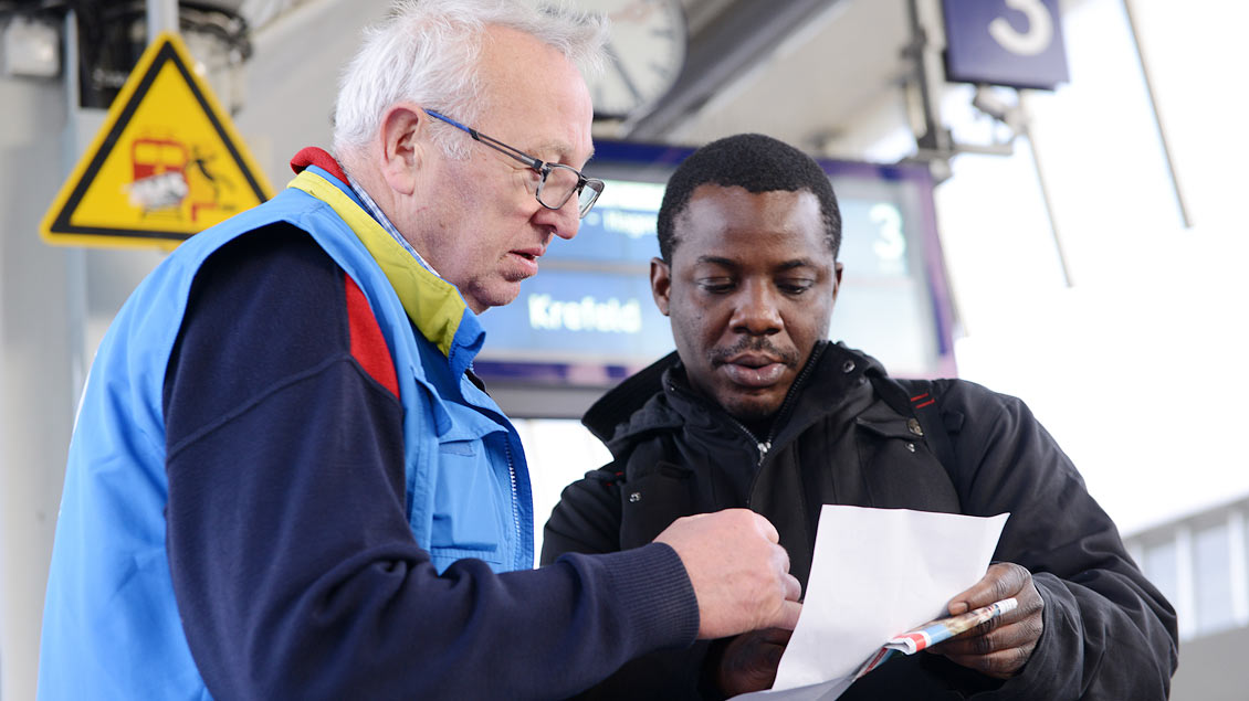 Ein ehrenamtlicher Mitarbeiter der münsterschen Bahnhofsmission hilft einem Reisenden bei der Weiterfahrt.