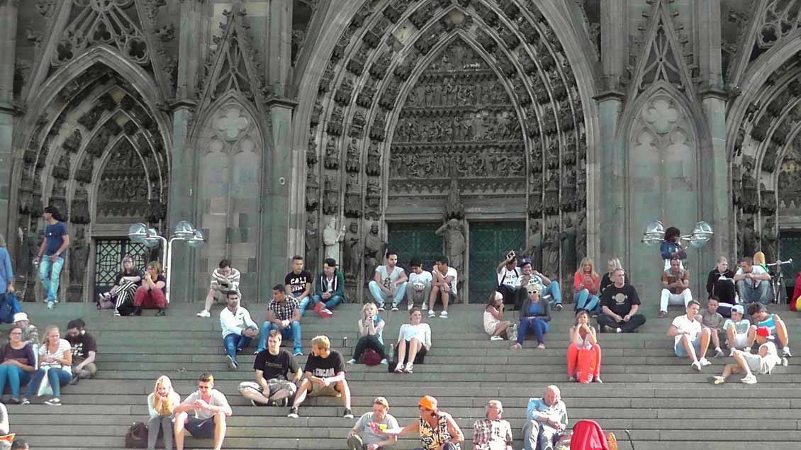 Menschen sitzen auf den Treppenstufen vor dem Kölner Dom.