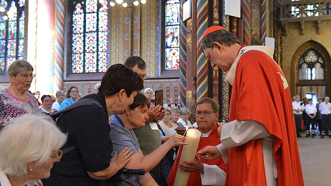 Kardinal Rainer Maria Woelki und Malteser Diözesanseelsorger Pfarrer Markus Polders entzünden gemeinsam mit einer Pilgerin die Kerze.