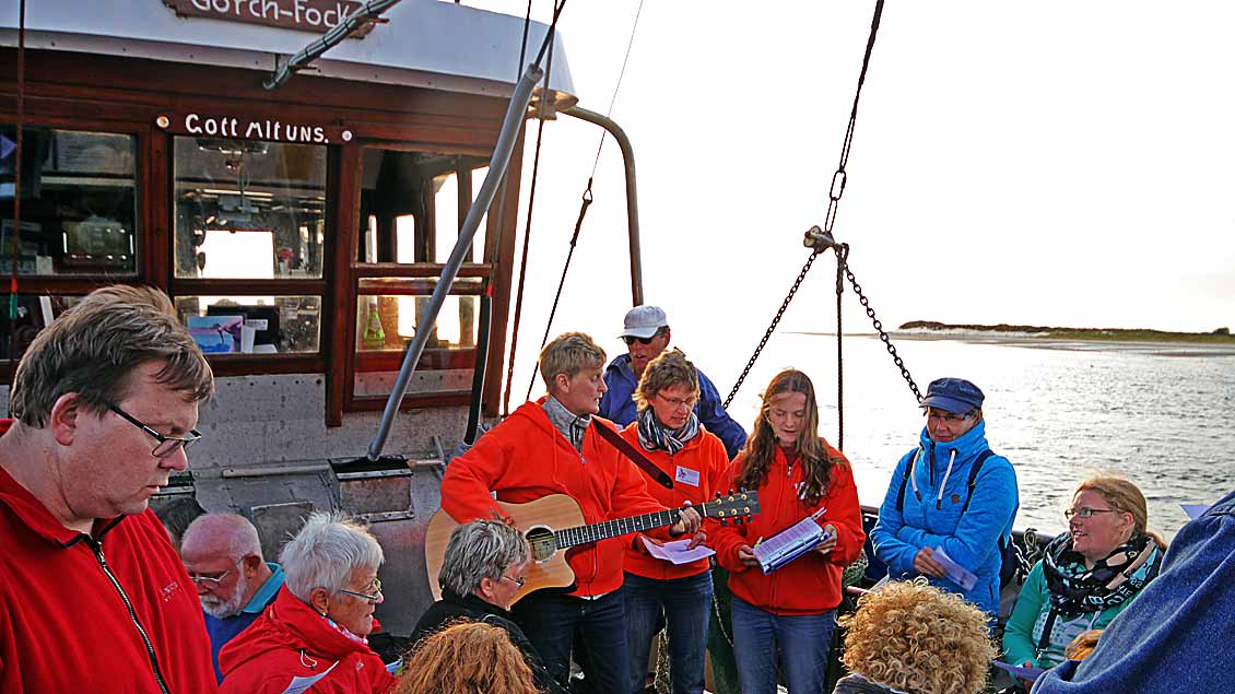 Urlauberseelsorgerin Heike Pendias (mit Gitarre) feiert zusammen mit 50 Urlaubern im Windschatten der Insel Spiekeroog an Bord des Krabbenkutters „Gorch Fock“ eine Abendandacht.