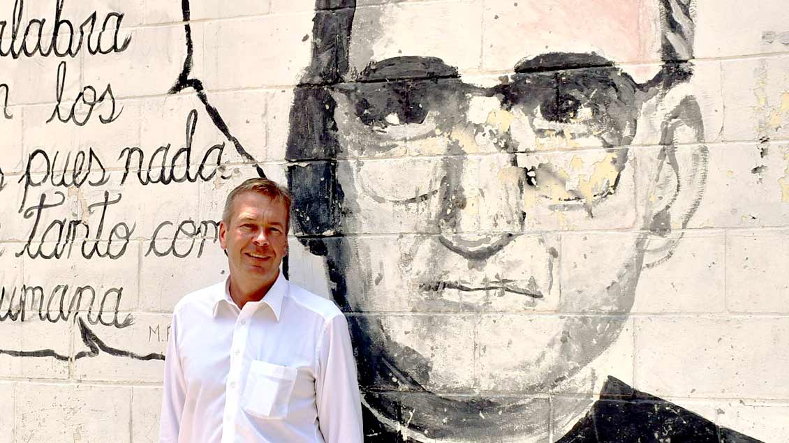 Bernd Finke, Botschafter der Bundesrepublik Deutschland in El Salvador, vor einem Mauerporträt des 1980 erschossenen Erzbischofs von San Salvador, Oscar Romero. Am 14. Oktober 2018 spricht in Papst Franziskus in Rom heilig.