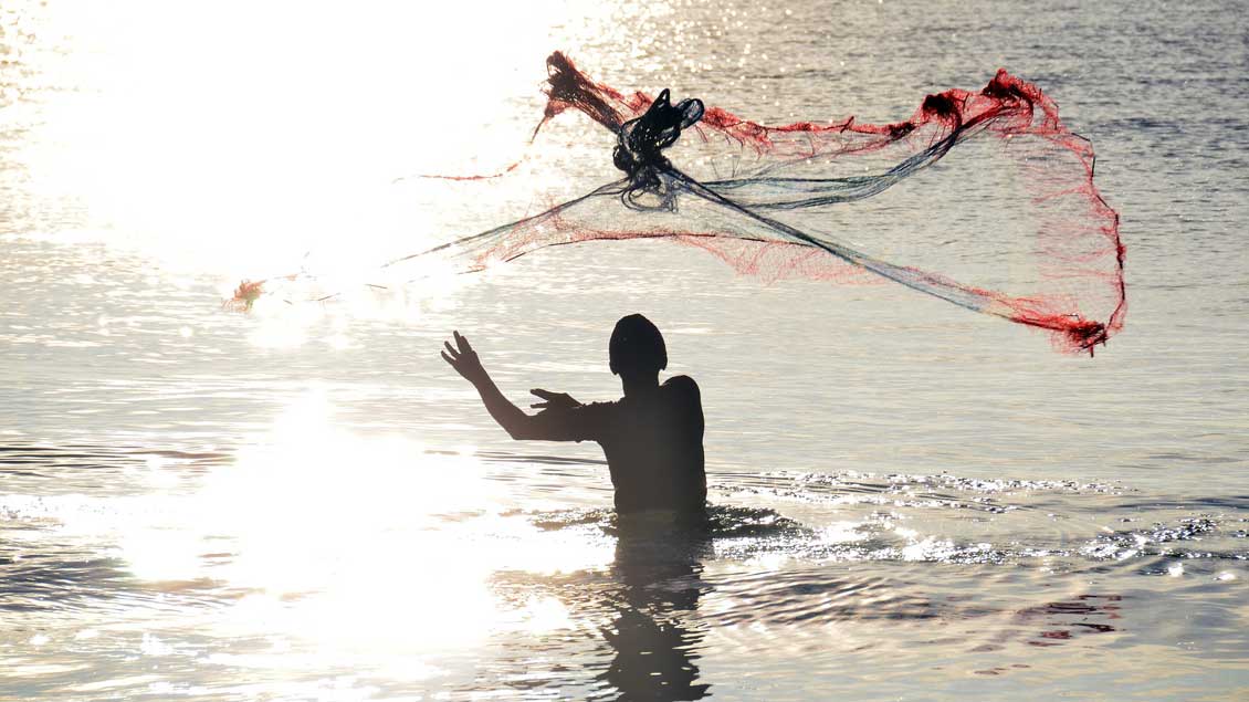 Ein Fischer steht im Wasser und wirft ein Netz aus.