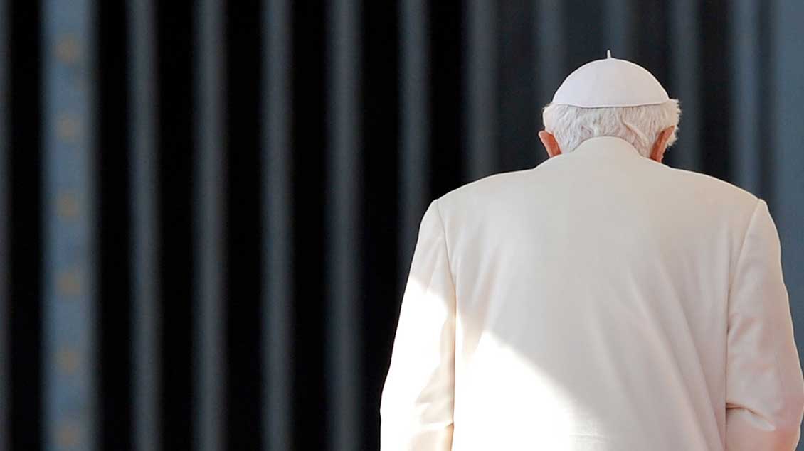 Der emeritierte Papst Benedikt XVI. vor einem Gitter von hinten fotografiert.
