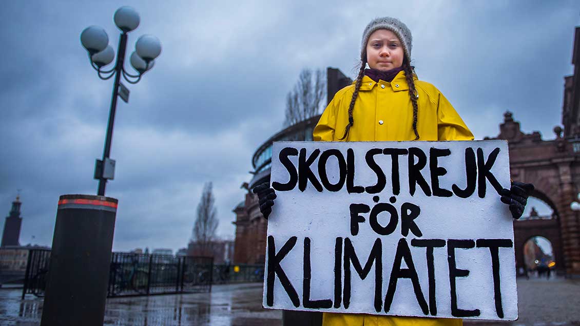 Greta Thunberg im gelben Regenmantel mit einem Schild "Schulstreik für das Klima".