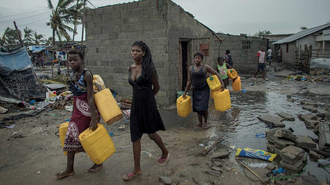 Frauen und Kinder tragen Wasser-Kanister durch ein überschwemmtes Dorf in Mosambik.