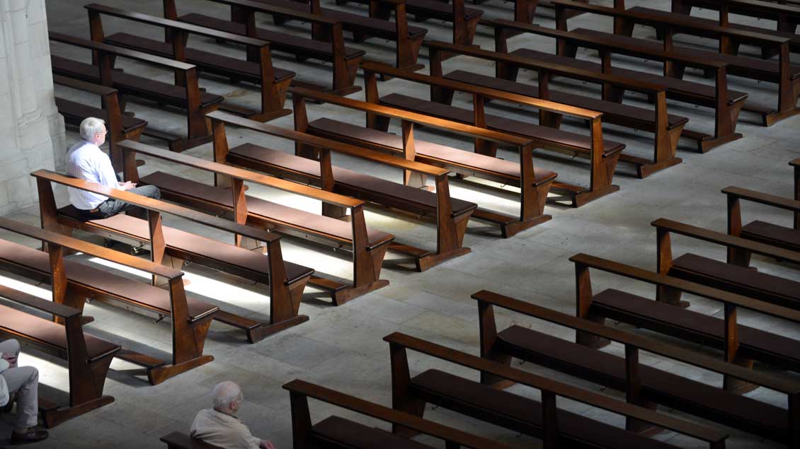Wenige Menschen sitzen in Kirchenbänken