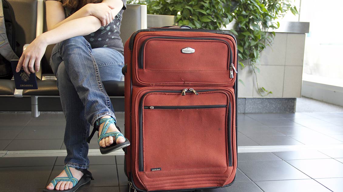 Junge Frau wartet mit ihrem Koffer am Flughafen.