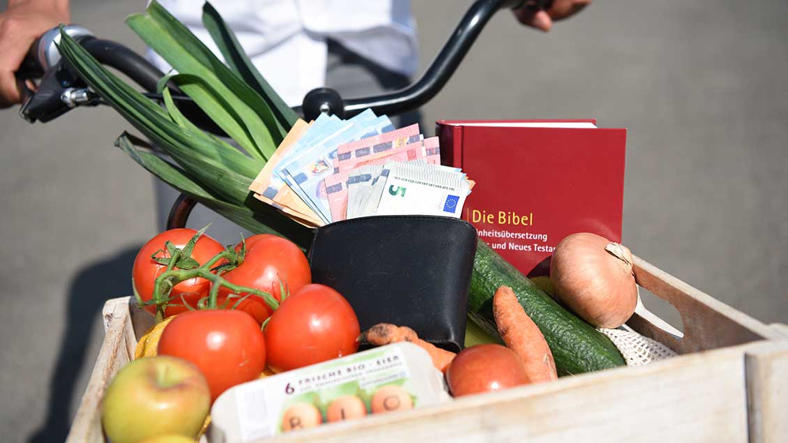 Korb mit Gemüse, Geld, Eiern und Bibel auf einem Fahrrad.