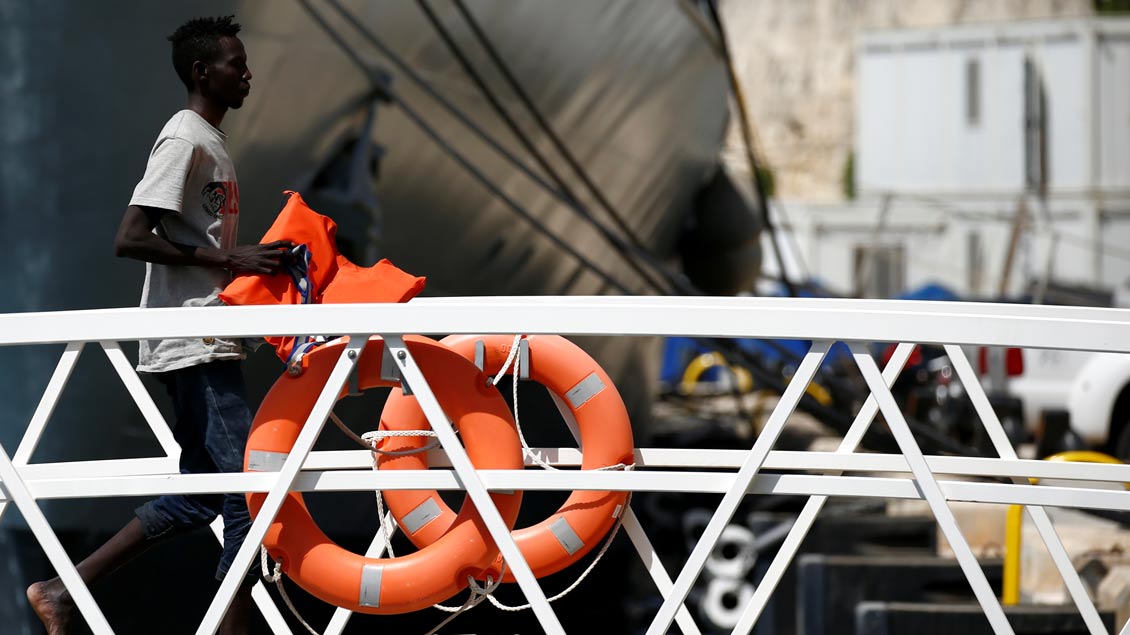 Ein farbiger Mann verlässt mit einer Rettungsweste ein maltesisches Militärboot.