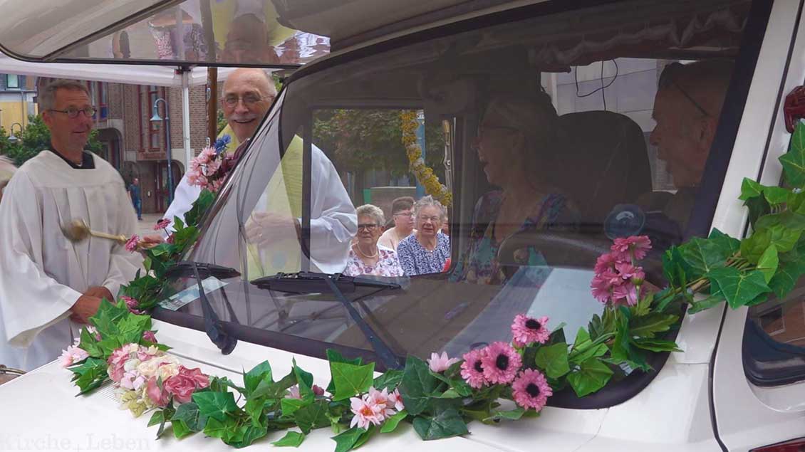 Pater Hans Peters steht am Fenster des Reisemobils und besprengt das Fahrzeug mit Weihwasser.
