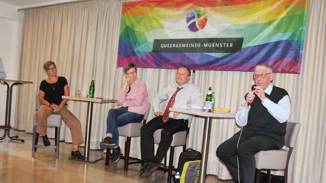 Vier Menschen diskutieren unter dem Banner der Queergemeinde Münster.