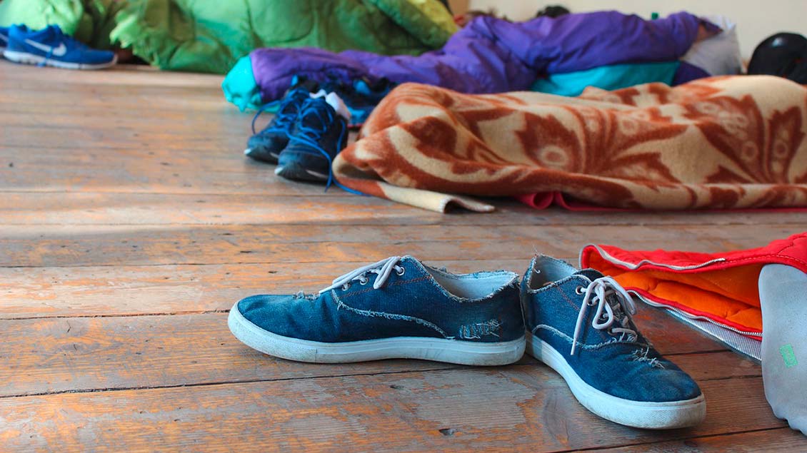 Schuhe und Schlafsäcke liegen auf einem Holzboden.