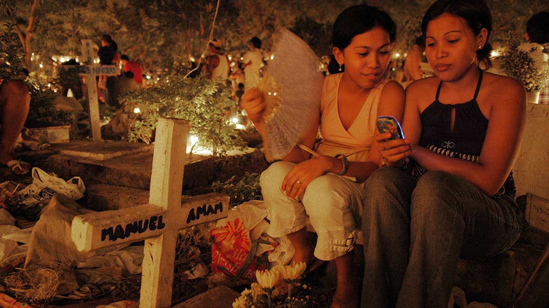 Zwei jungen Frauen sitzen am Grab eines Verwandten auf einem Friedhof Friedhof in Cebu-City auf den Philippinen.
