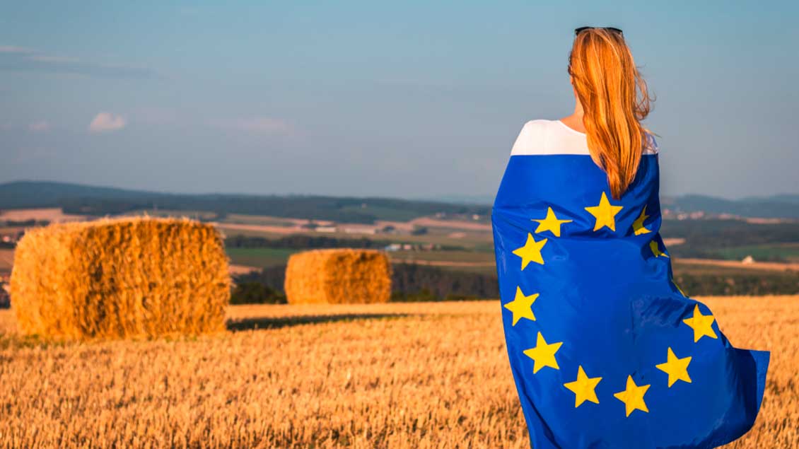 Frau mit Europa-Fahne auf einem abgteernteten Getreidefeld