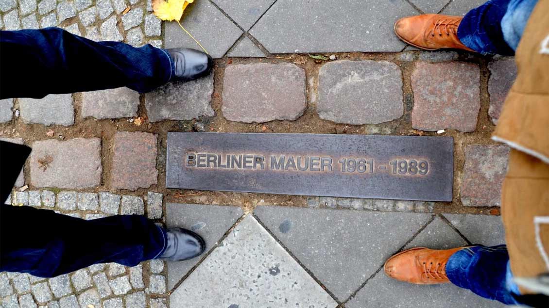 zwei paar Füße von oben fotografiert, dazwischen verläuft eine Gedenklinie zur Berliner Mauer.