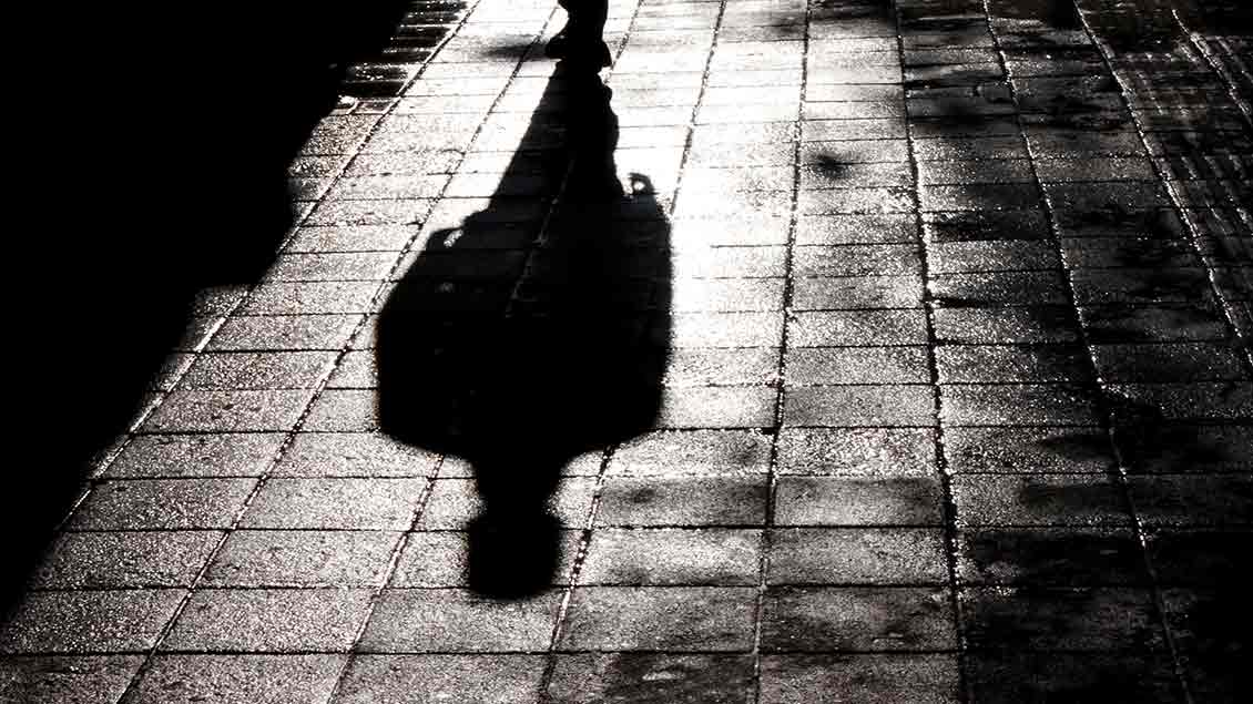 Der Schatten eines Mannes fällt auf eine dunkle Straße.