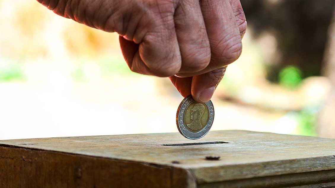 Eine Hand steckt eine Münze in eine Spendenbox