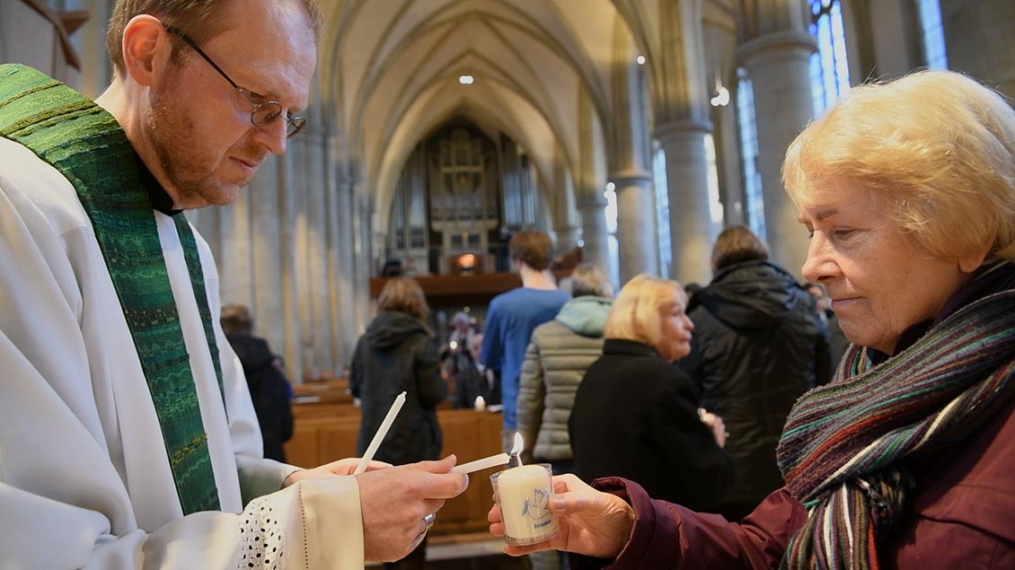 Stadtdechant Hagemann entzündet beim Friedensgebet in Münster die Kerze einer Gottesdienstteilnehmerin.