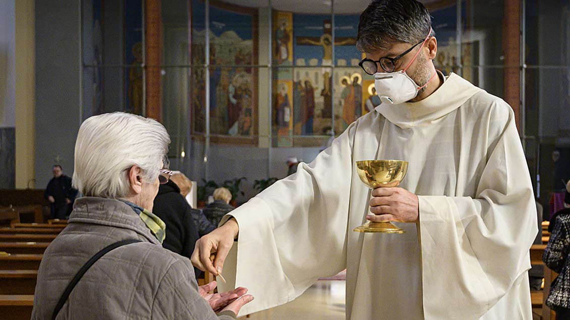 Ein Priester mit Mundschutz spendet in Rom einer Frau die Kommunion