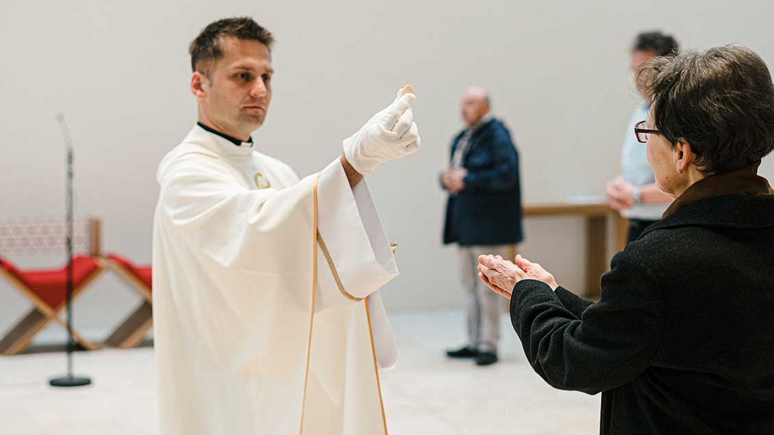 Priester spendet mit Handschuhen die Kommunion
