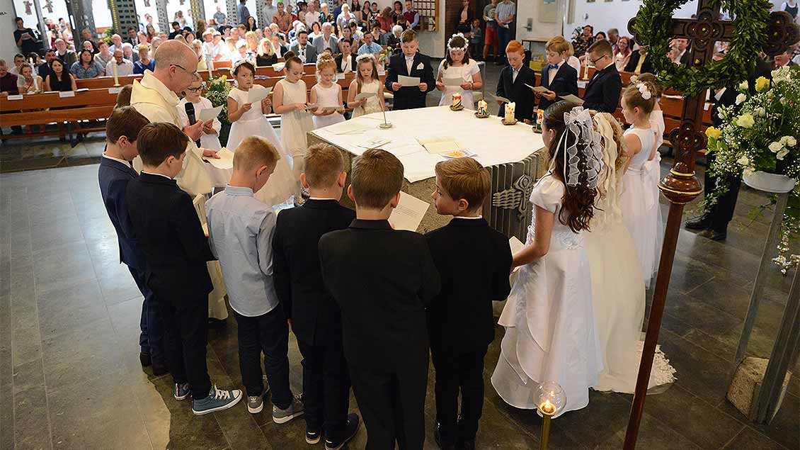 Um einen Altar stehen Erstkommunionkinder mit dem Priester und halten sich an den Händen.