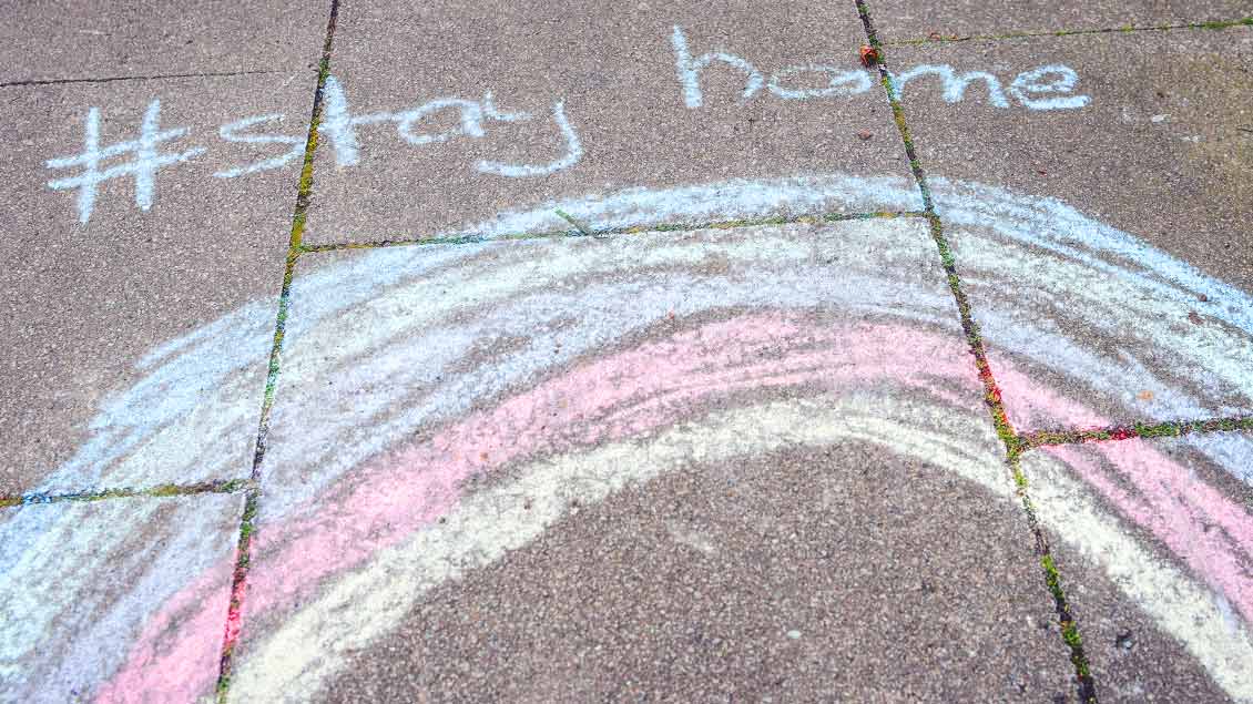 Auf einem Bürgersteig ist mit Kreide ein Regenbogen aufgemalt. Darüber steht "#stay home"