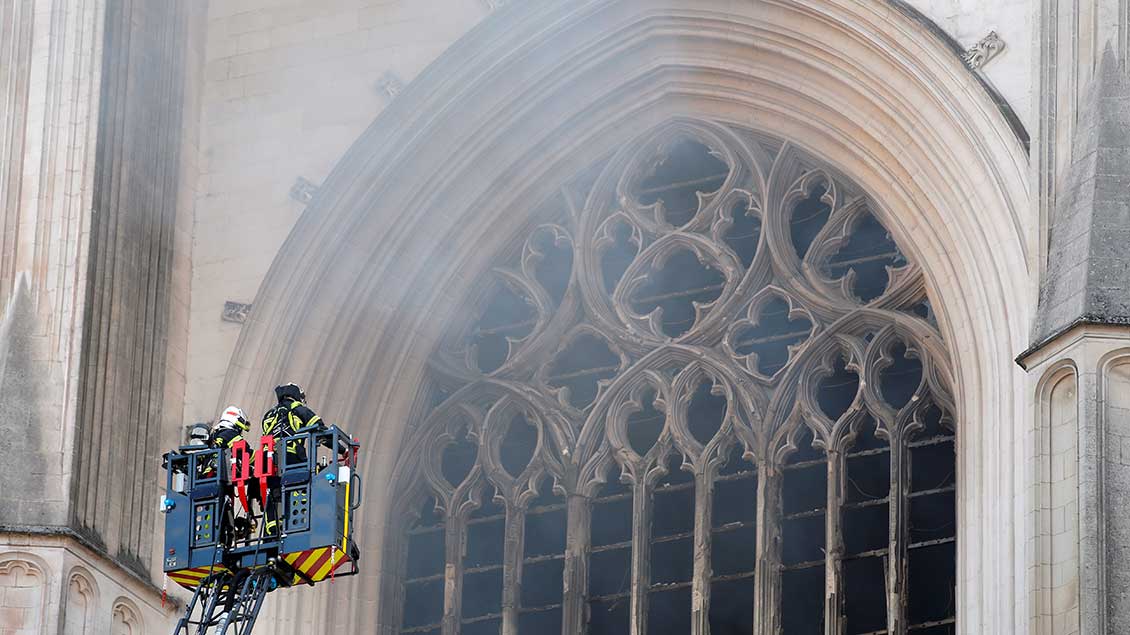 Feuerwehrleute vor einem Fenster der brennenden Kathedrale von Nantes