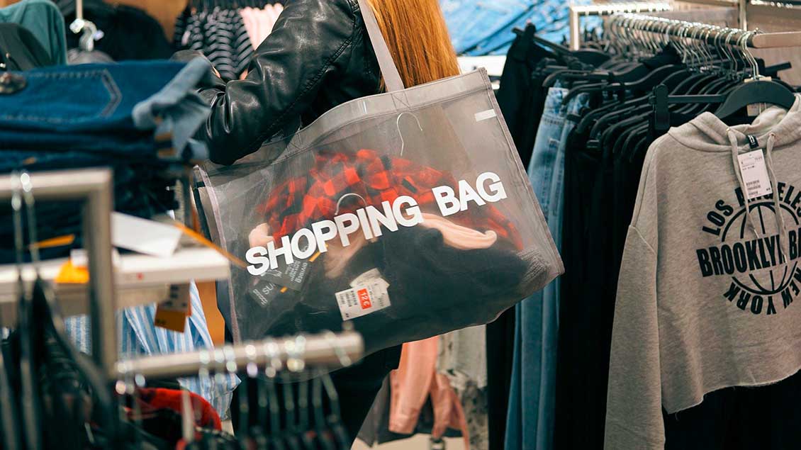 Frau mit einer großen Einkaufstasche mit der Aufschrift "Shopping Bag" in einem Bekleidungsgeschäft.
