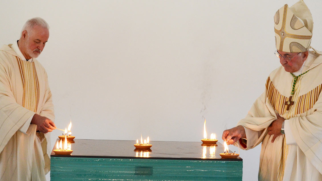 Pfarrer Lunemann und Bischof Genn entzünden Feuerschalen auf dem Altar.