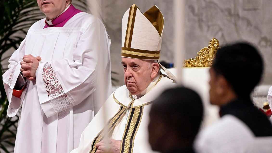 Der Papst sitzt mit einer Mitra auf dem Kopf auf einem Stuhl. Um ihn herum stehen Messdiener.