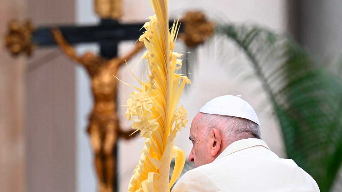 Mit einem Palmzweig in der Hand schaut Papst Franziskus sitzend auf das Kreuz