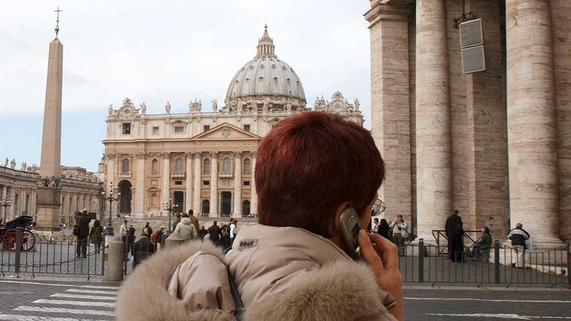 Eine Frau telefoniert mit dem Handy vor dem Petersdom in Rom