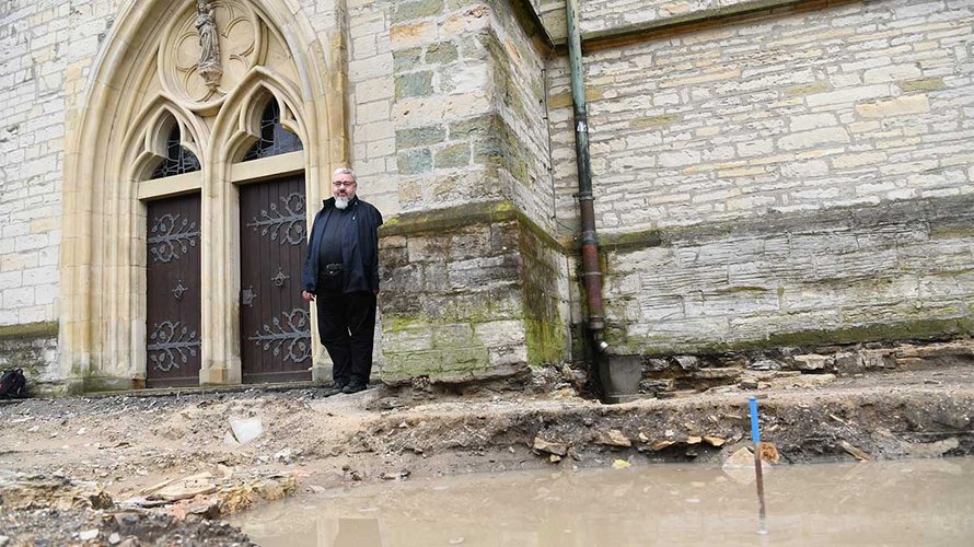 Pfarrer Irmgedruth vor einem vollgeregneten Ausgrabungsbereich an der Westseite der Kirche. | Foto: Michael Bönte