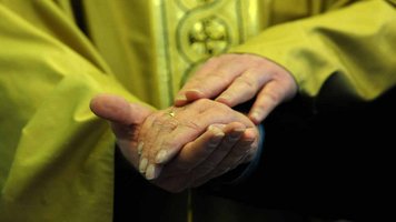 Priester hält die Hand einer Frau mit Ehering