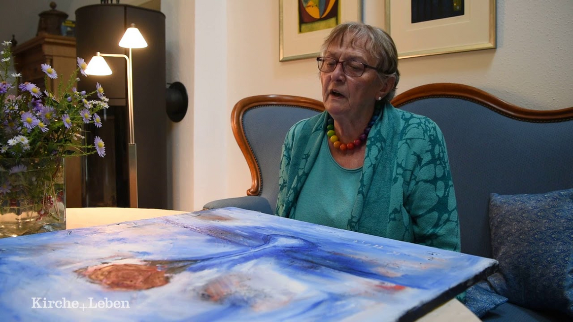 Margret Pernhorst sitzt auf ihrem Sofa und betrachtet ihr Rosenbild.