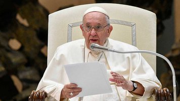 Papst Franziskus sitzt vor einem Mikrofon