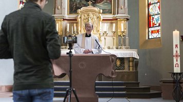 Ein Priester wird am Altar per Smartphone gefilmt.