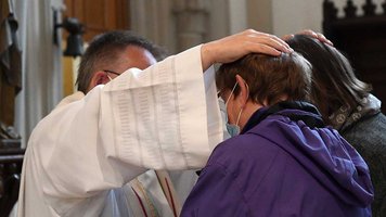 Ein Priester legt zwei Frauen die Hände auf die Köpfe