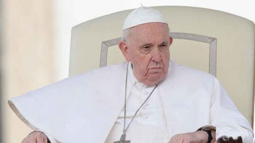 Papst Franziskus sitzt auf einem Stuhl in weißem Gewand
