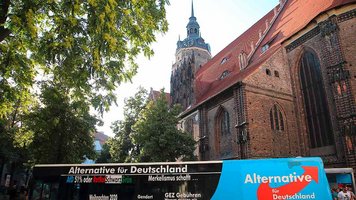 Symbolfoto einer Kirche in Brandenburg an der Havel mit einem AfD-Wahlkampfbus