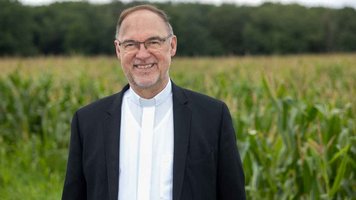Weihbischof Rolf Lohmann steht vor einem Maisfeld
