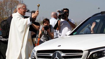 Ein Priester segnet ein Auto mit Weihwasser
