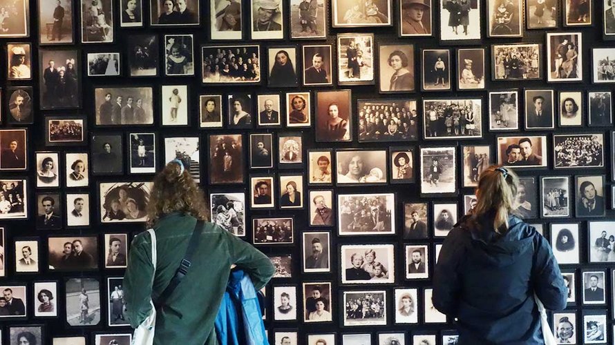 Reise-Teilnehmer vor der Foto-Wand mit Bildern der Holocaust-Opfer.