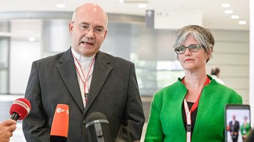 Bischof Helmut Dieser und Birgit Mock sprechen in Mikrofone