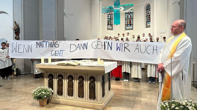 Messdiener halten an einem Altar das Banner "Wenn Matthias geht, dann geh´n wir auch" hoch.