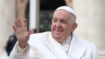Papst Franziskus lächelt leicht und winkt.