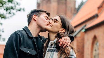 Ein Mann küsst eine Frau, im Hintergrund is eine Kirche zu sehen.