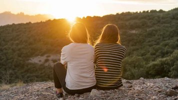 Zwei junge Frau sitzen auf einem Felsen und blicken auf einen Sonnenuntergang