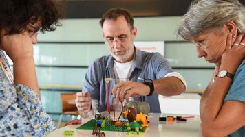 Drei Erwachsene bauen mit Legosteinen